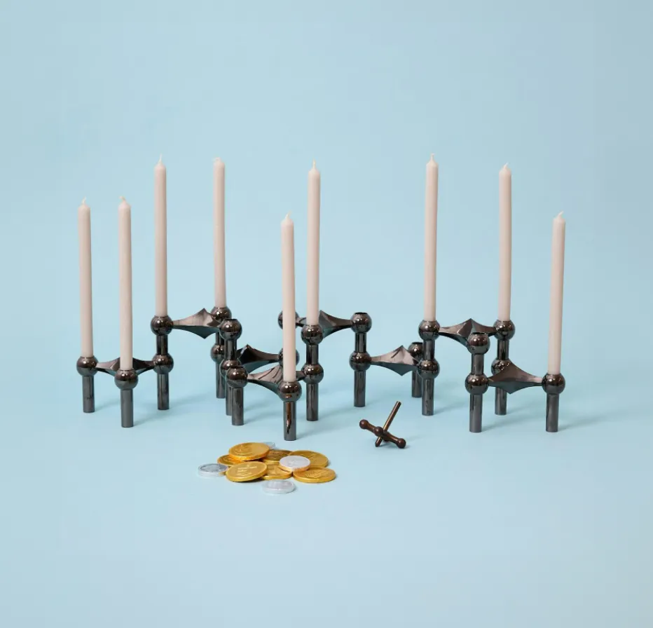 Modern Hanukkah menorah with white candles, gold and silver gelt coins, and a small dreidel on a light blue background.