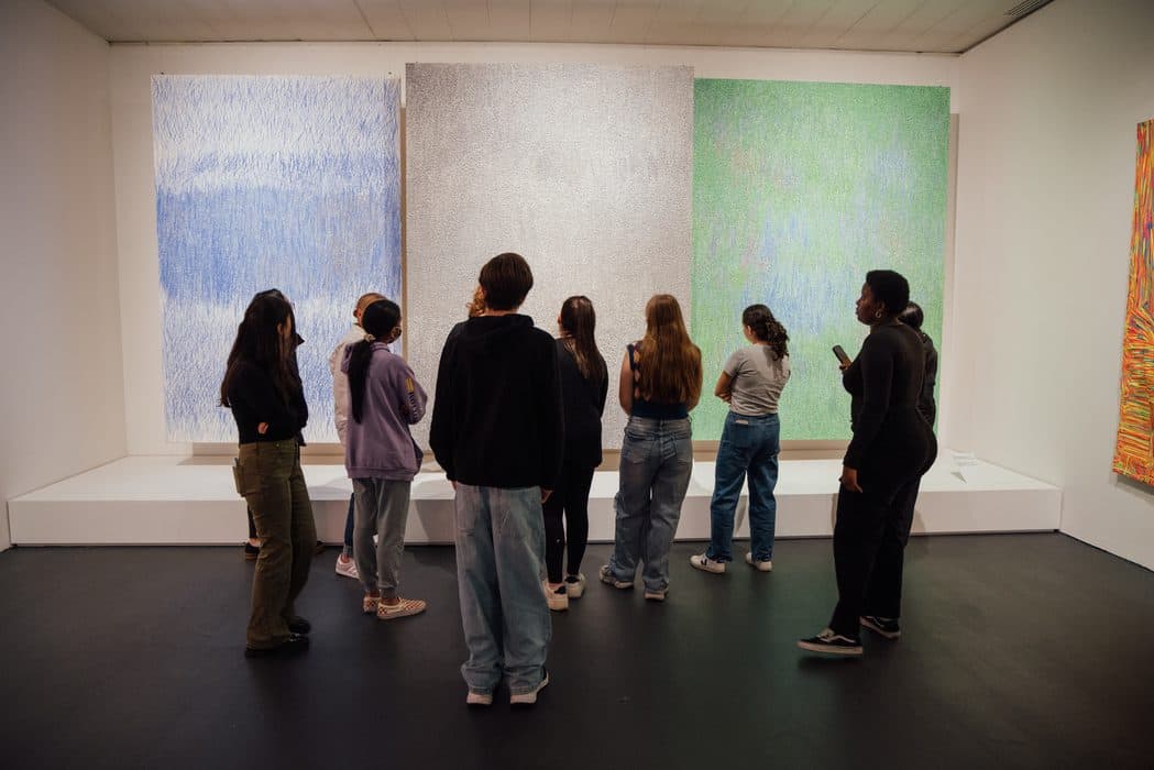 Group of teens standing in front of large abstract paintings with blue, silver, and green tones during a museum program.