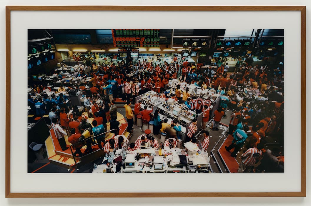 g: THE STOCK EXCHANGE, ECONOMIC HISTORY

Andreas Gursky
Singapore Stock Exchange, 1997
Chromogenic print, face-mounted to acrylic
Solomon R. Guggenheim Museum, New York, Purchased with funds contributed by the Photography Committee, 1998

The photographs of Andreas Gursky offer a scintillating tension between abstraction and reality in all its teeming detail. A shift from the concrete to the abstract is a hallmark of late capitalist society. Money is an abstraction of value. Debt is an abstraction of money. Stocks and bonds are abstractions of abstractions, their connections to tangible things—corn to eat, wood to build houses— reduced to the buzz of binary code through fiber-optic cables. Gursky’s photographs, on the one hand, convey vividly the inhuman scale and compulsive regularity of the organs of our economy. On the other hand, they expose their own status as images, as objects, by pruning and polishing reality to a painful sheen.

Benjamin saw the stock exchange as a linchpin in the collective mythology of capitalism: swarms of people, furiously busy, their inscrutable activities determining the fate of the world.