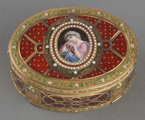 An ornate oval snuff box with gold trim and intricate decorative patterns. The lid features a central enamel portrait of a woman in 18th-century attire, framed by concentric rows of pearls and gold filigree. The background of the lid is deep red with gold star-like accents, divided by gold bands with small pearls at intersections. The sides of the box continue the red and gold motif with floral and geometric designs, including green enamel leaves around the upper edge.