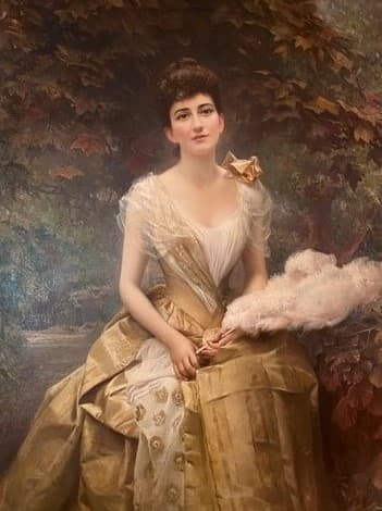 Oil portrait of a seated woman outdoors, positioned in front of a tree with autumn leaves. She has dark hair styled up and wears a golden gown with white lace detailing and floral embroidery. A soft pink plume or fan rests in her lap, held gently in her hands. The setting suggests a garden or park, with soft, muted lighting and a warm color palette.