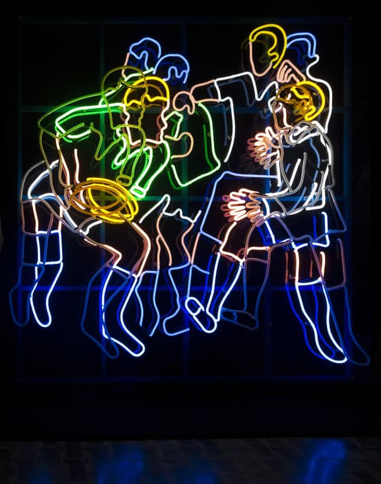 Colorful neon light artwork depicting an overlapping group of rugby players in motion, outlined in yellow, green, blue, pink, and white lights against a dark background.