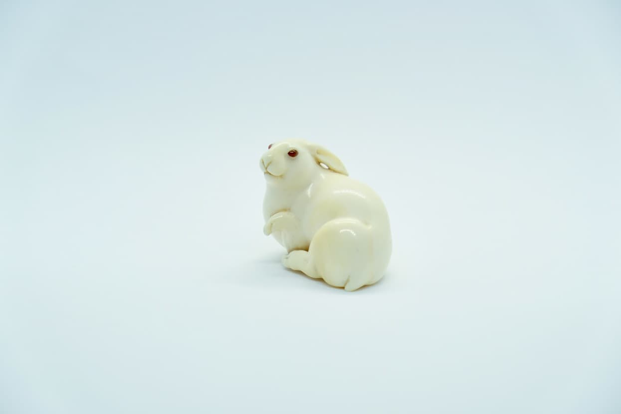 Small ivory or ivory-colored carved figure of a rabbit, sitting on a white background.