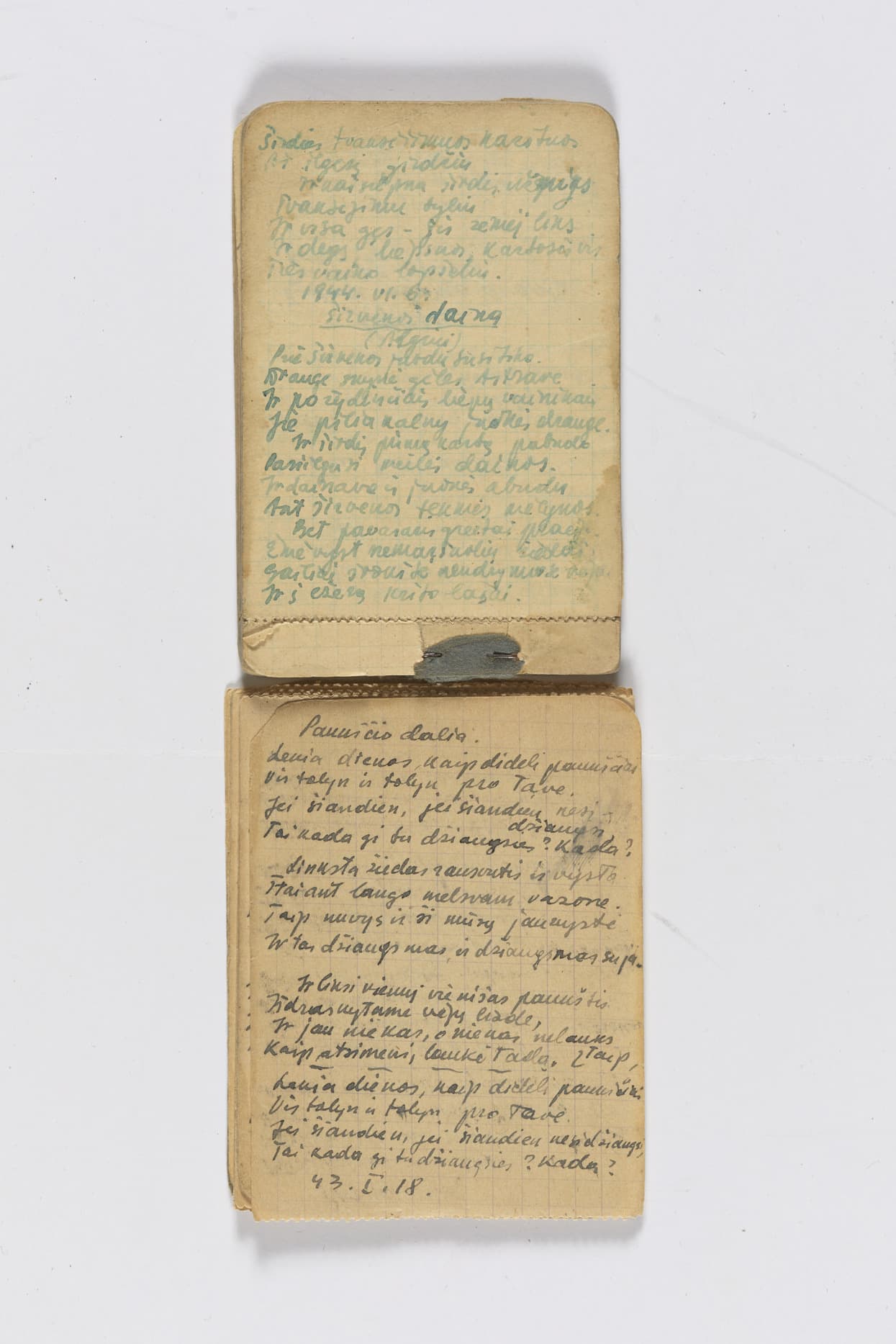 Two small notebook pages with handwritten text in blue and black ink, written in a neat cursive script on yellowed grid paper. The upper page has faded text, while the lower page is darker and more legible.