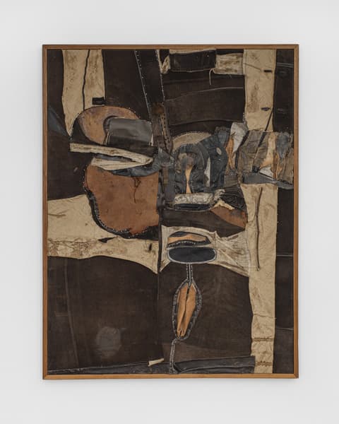 Mixed-media abstract artwork composed of layered, stitched, and collaged dark brown, beige, and black fabric pieces. The composition has a highly textured surface with visible seams, rough edges, and organic shapes, framed in a simple wooden frame against a white background.