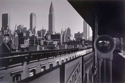 Black and white photograph of New York City skyline with the Chrysler Building prominently in view; in the foreground is a rooftop observation deck with coin-operated binoculars and vintage advertisements.