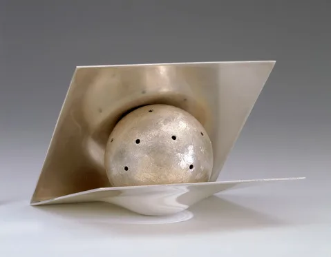 Modern silver spice container shaped as a geometric composition with a perforated sphere partially enclosed by two angled, intersecting flat planes.