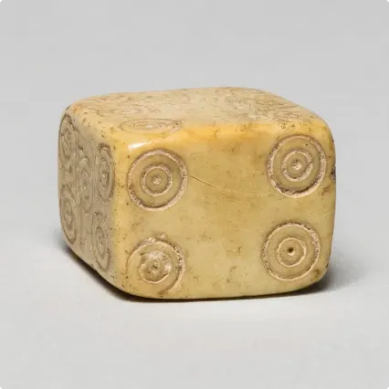 Ivory die with circular dot patterns carved on each side, shown resting on a light gray surface.