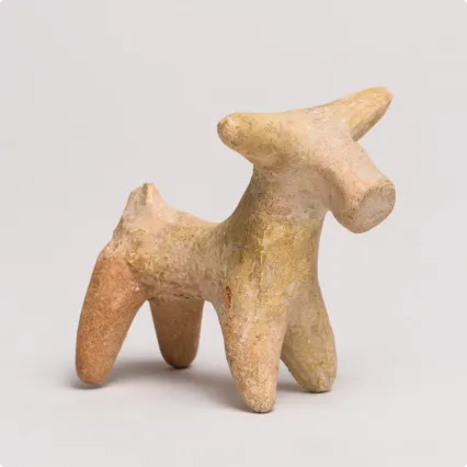 Small terracotta figurine of a stylized animal with four legs, a short tail, and pointed head, possibly representing a bull or deer, on a plain light background.