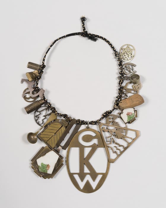A charm bracelet on a black chord, with charms layered and laid flat in a circle. In the center the largest is a brass 