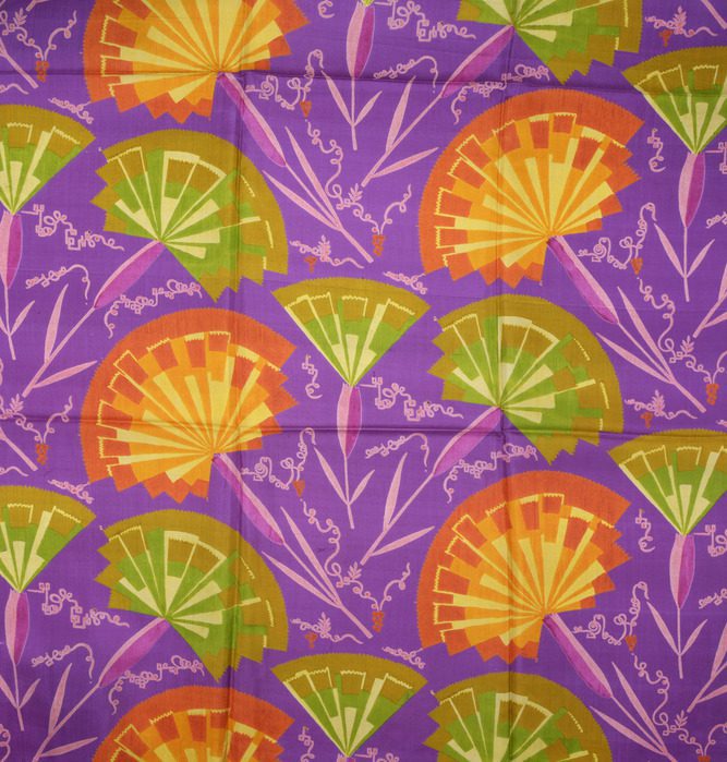 Patterned textile with repeating orange and green fan-shaped flowers on a vivid purple background. Light purple grapevines are scattered playfully between the flowers.